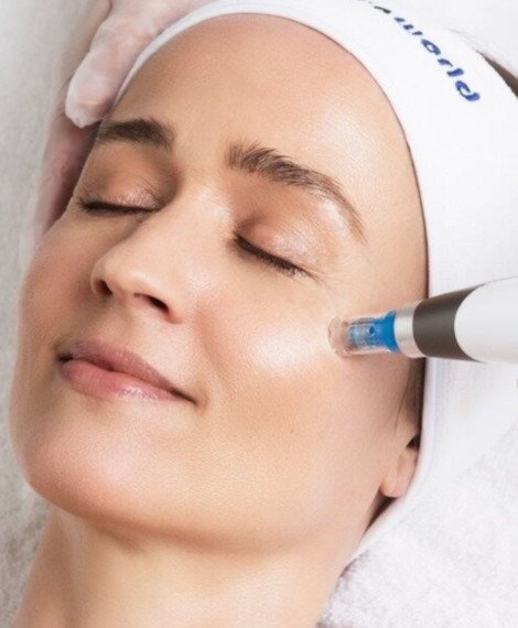 En person med slutna ögon får en hudvårdsbehandling med en apparat på kinden på ett spa, iförd ett vitt pannband.