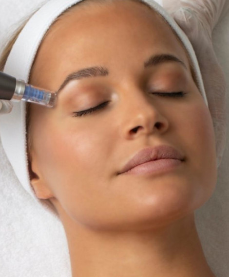 Person som får en hudvårdsbehandling med en handhållen enhet nära ögonbrynet, bär ett vitt pannband, slutna ögon, liggande på en behandlingssäng.