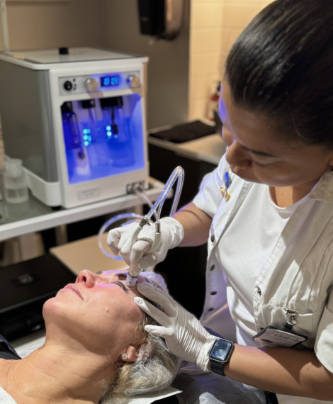 En kvinna får en ansiktsbehandling av en professionell som använder specialutrustning i en klinikmiljö.